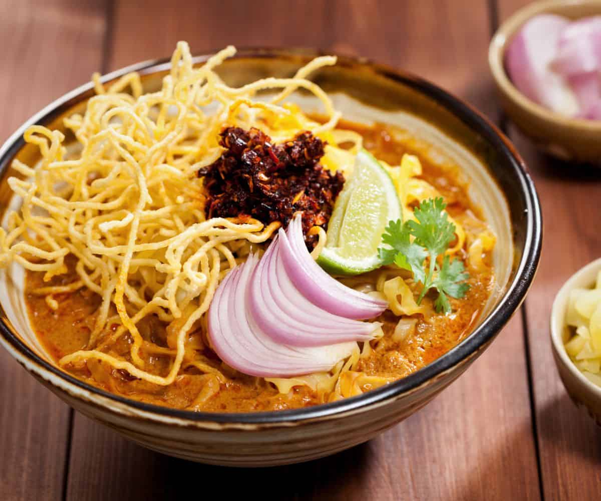 a bowl of khao soi with shallots, lime wedge, cilantro and fried chilies garnish