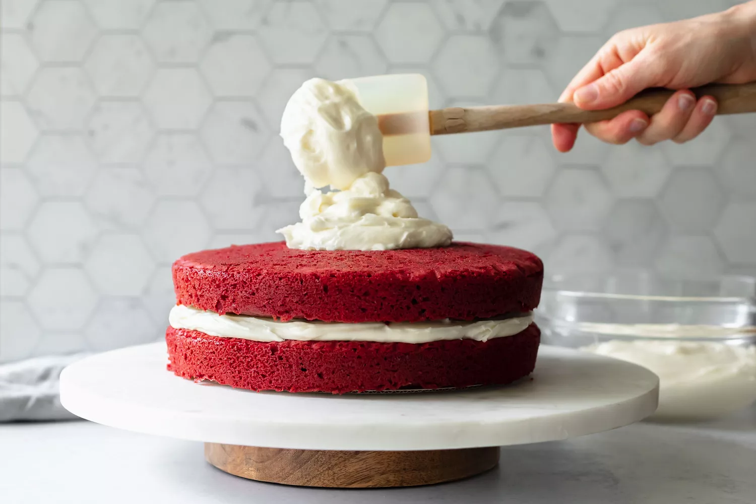 dolloping cream cheese frosting on top of red velvet cake layers